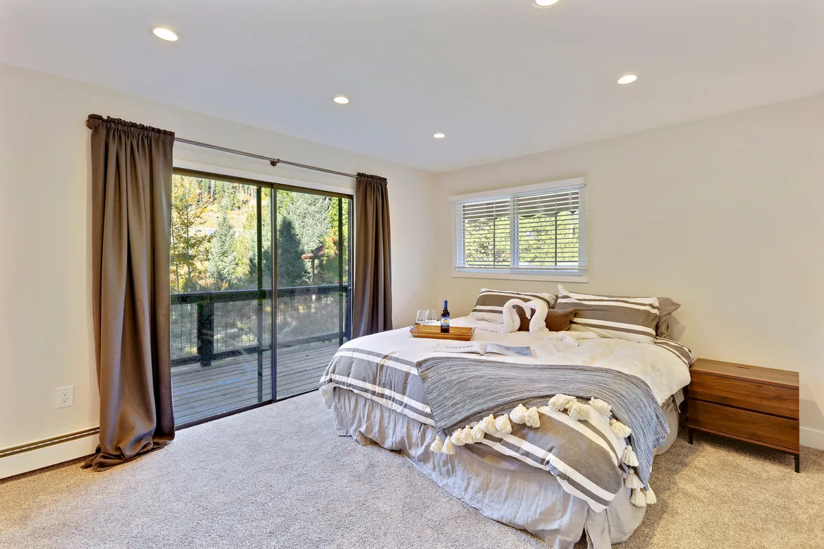 A serene king-sized bedroom featuring a plush bed with premium linens, sliding glass doors that offer views of the natural surroundings, and a wooden nightstand. The space is bathed in natural light, contributing to a restful and inviting atmosphere.