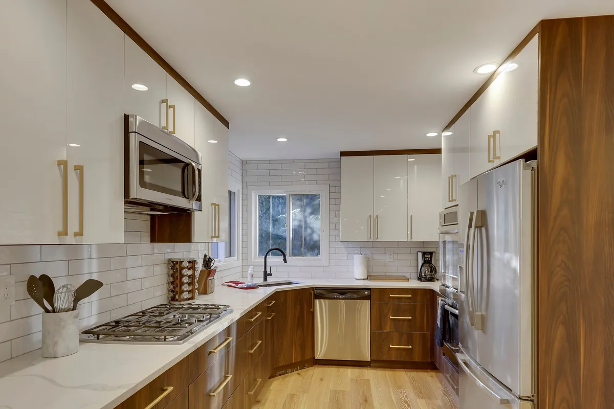 A modern chef’s kitchen featuring stainless steel appliances, a spacious quartz countertop, gold hardware, and a white subway tile backsplash. The space exudes a contemporary and welcoming vibe, ideal for cooking and entertaining.
