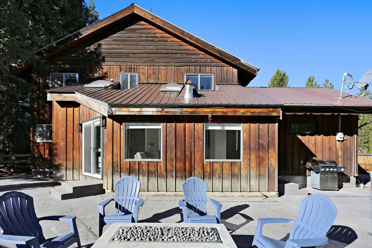 The wooden exterior of the chalet is complemented by blue Adirondack chairs and a fire pit, inviting guests to enjoy casual gatherings, sunsets, and starlit evenings in a private setting.