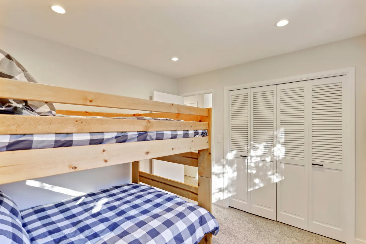 A cozy bunk bedroom with checkerboard bedding and closet doors. The room's playful vibe is perfect for children or group sleepovers, and it evokes a sense of fun and togetherness.