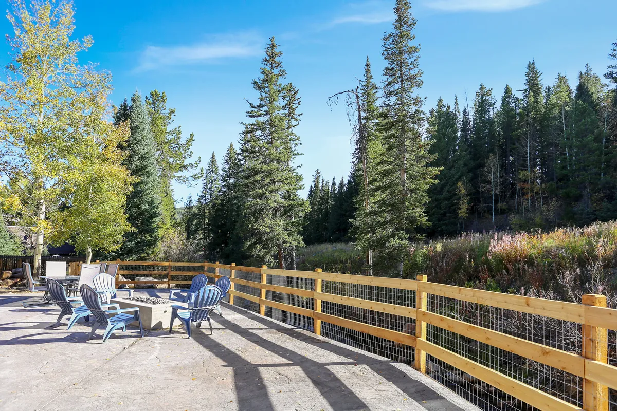 A tranquil backyard scene featuring Adirondack chairs encircling a fire pit, with a wooden fence and trees in the background. The area is ideal for stargazing, nature walks, or warming up after winter activities.
