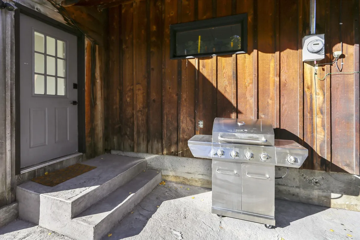A functional and inviting outdoor grilling area, with a grill set against a wooden wall and a doorway leading inside, perfect for al fresco dining and casual celebrations.
