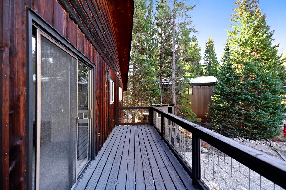 A peaceful wooden deck surrounded by trees, with a sliding glass door connecting the interior to the outside. The deck offers space for relaxation and peaceful enjoyment of the natural environment.