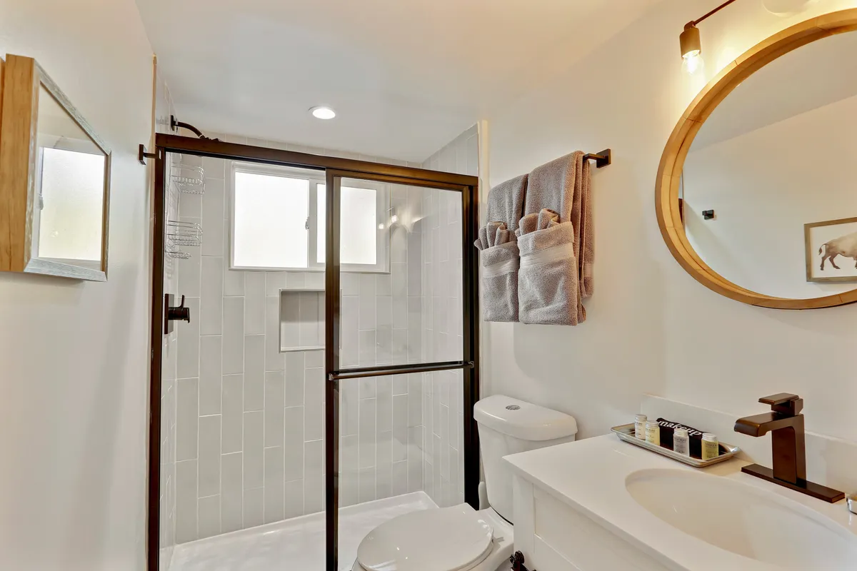A sparkling, modern bathroom with a large round mirror, glass-door shower, stylish sink, and neatly arranged towels. The setting is fresh, clean, and designed for relaxation and self-care.