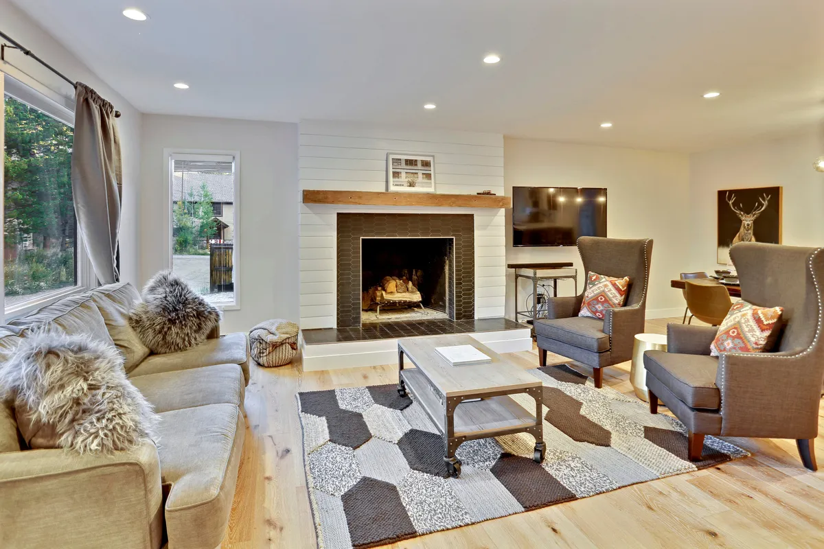 This inviting living room features a crackling fireplace surrounded by plush sofas and armchairs, set atop a cozy rug, creating the perfect space for guests to gather, relax, and enjoy the warmth after a day on the slopes.